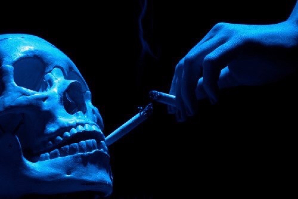 AN IMAGE SHOWING A SKELETON SMOKING A CIGARETTE, IMPLYING THAT EVEN AFTER DEATH WE WILL INDULGE IN THAT WHICH KILLS US. MUCH LIKE THE PERSON I WAS